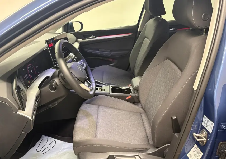 Vue intérieure côté conducteur de la Volkswagen Golf 1.5 eTSI 116 DSG7 Bleu Anémone, avec sièges tissu gris et tableau de bord numérique.
