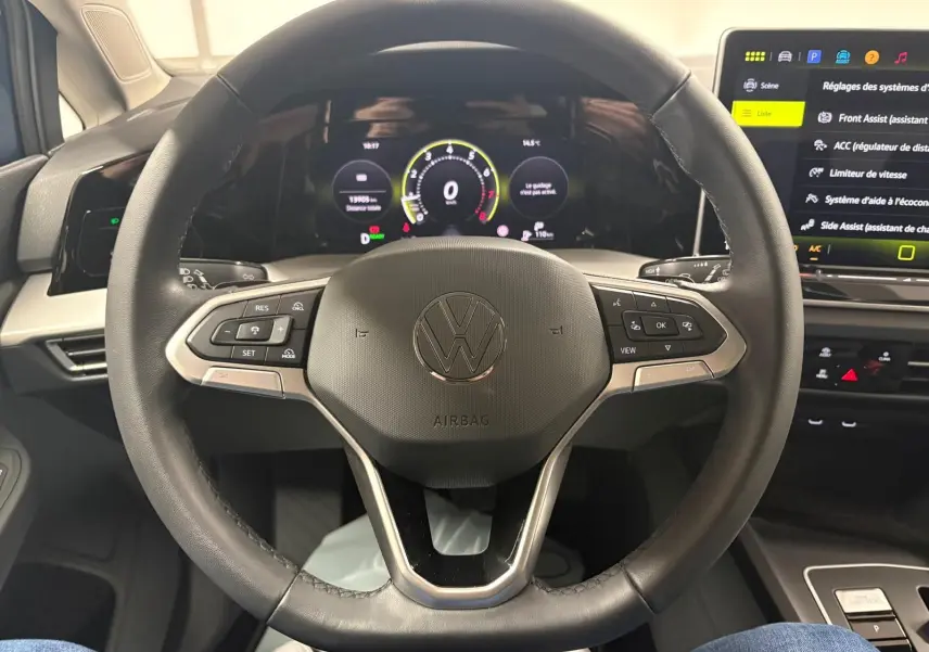 Vue rapprochée du volant multifonction noir de la Volkswagen Golf 1.5 eTSI 116 DSG7 avec tableau de bord numérique allumé.