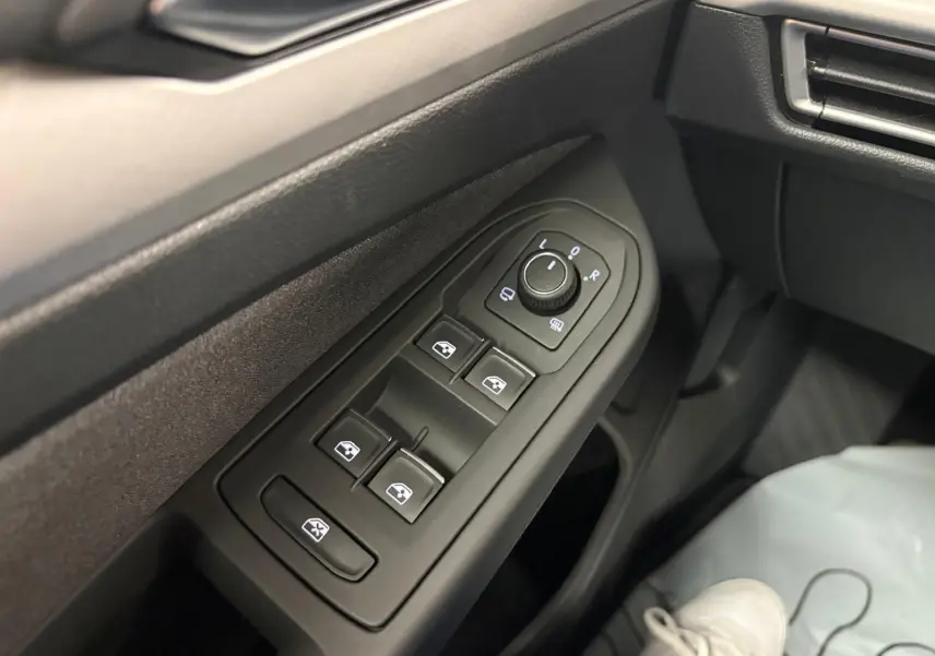 Gros plan sur les commandes des vitres électriques et des rétroviseurs côté conducteur dans l’habitacle noir d’une Volkswagen Golf 2025.