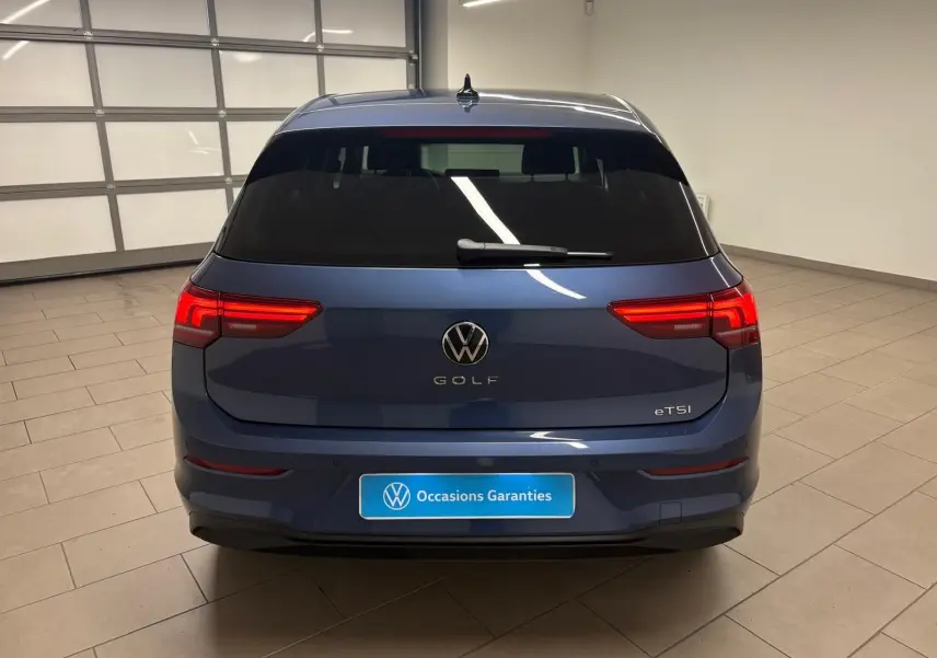 Vue arrière d'une Volkswagen Golf 1.5 eTSI 116 DSG7 en bleu Anémone avec feux arrière allumés dans un garage.