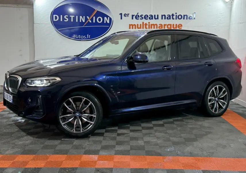BMW X3 xDrive30e bleu en profil côté gauche dans un showroom avec logo Distinxion en arrière-plan.