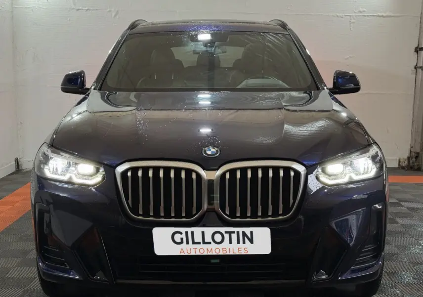 Vue frontale d'un BMW X3 xDrive30e bleu avec phares LED allumés dans un garage.