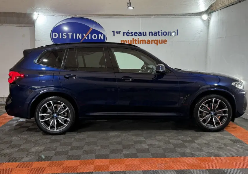 BMW X3 xDrive30e bleu en vue profil côté gauche, avec jantes alliage et vitres teintées dans un showroom.