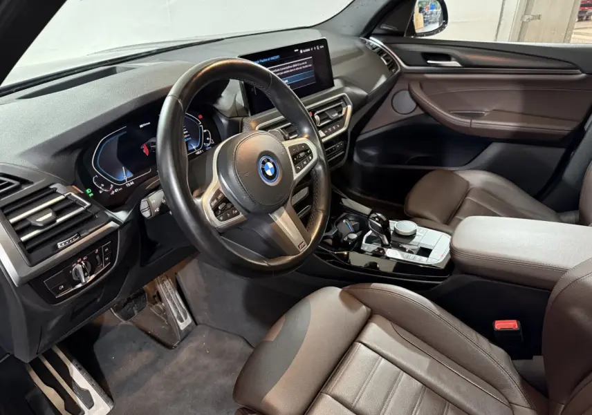 Intérieur BMW X3 xDrive30e 2023 vu côté conducteur, volant cuir, tableau de bord digital et console centrale noire brillante.