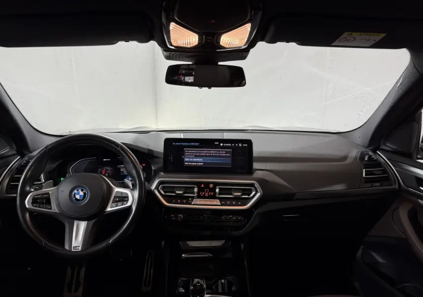 Intérieur BMW X3 xDrive30e 2023 vu de face, tableau de bord noir avec écran tactile central et volant cuir M Sport.