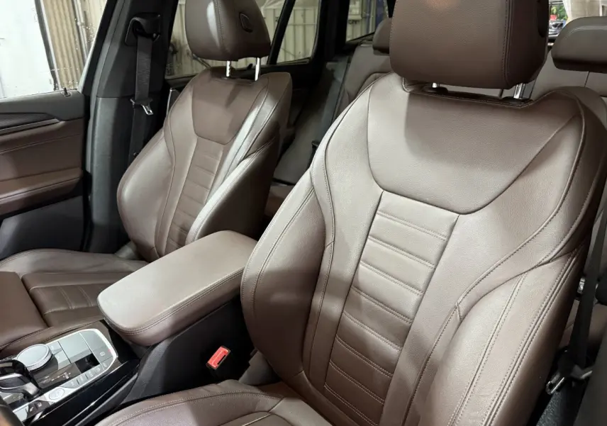 Gros plan sur les sièges avant en cuir marron du BMW X3 xDrive30e 2023, avec console centrale et commandes visibles.