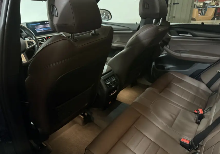 Intérieur arrière de BMW X3 bleu 2023, sièges cuir marron, console centrale avec aérateurs et commandes climatisation.