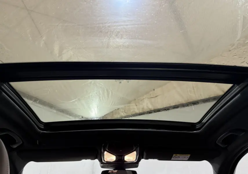Toit ouvrant panoramique en verre vu de l'intérieur d'un BMW X3 bleu xDrive30e 2023, éclairage intérieur allumé.