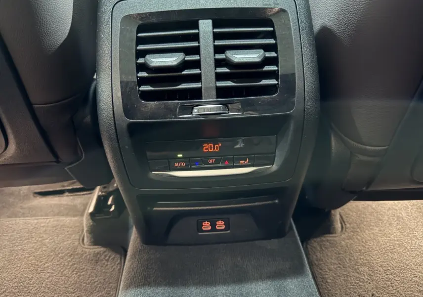 Détail de la console arrière noire du BMW X3 xDrive30e 2023 avec ventilation et commandes climatisation à 20°C.