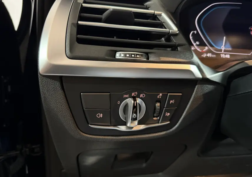 Gros plan sur le tableau de bord côté gauche du BMW X3 bleu 2023, montrant les commandes des phares et la ventilation.