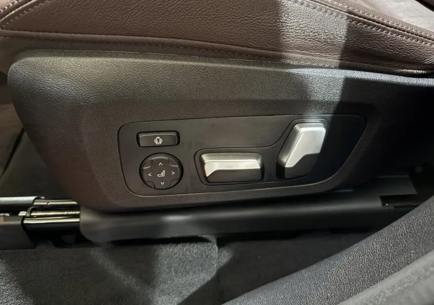 Gros plan sur les commandes électriques argentées du siège avant en cuir marron d'un BMW X3 bleu hybride rechargeable 2023.