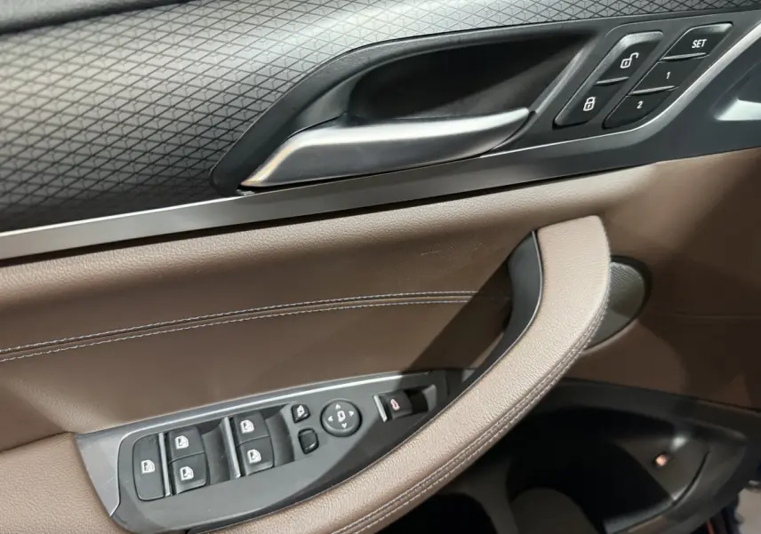 Détail de la porte côté conducteur du BMW X3 xDrive30e 2023 avec commandes de vitres et cuir marron.