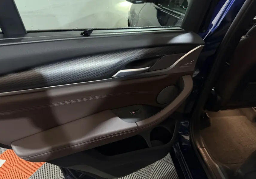 Intérieur de la porte arrière droite du BMW X3 xDrive30e bleu 2023, avec garniture cuir marron et détails noirs.