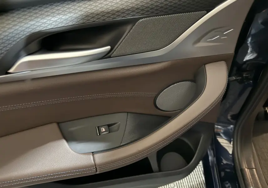 Détail de la portière avant gauche bleu foncé du BMW X3 xDrive30e avec garniture cuir marron et bouton de verrouillage.