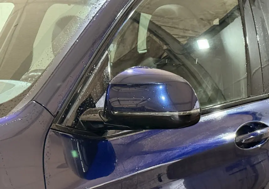 Gros plan sur le rétroviseur côté gauche d'un BMW X3 xDrive30e bleu 2023 avec gouttes d'eau visibles sur la carrosserie.
