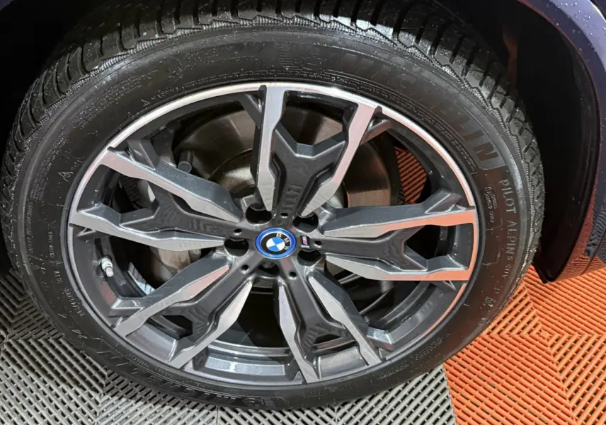 Gros plan sur la jante alliage sombre à motifs géométriques du BMW X3 bleu 2023 avec logo central BMW.