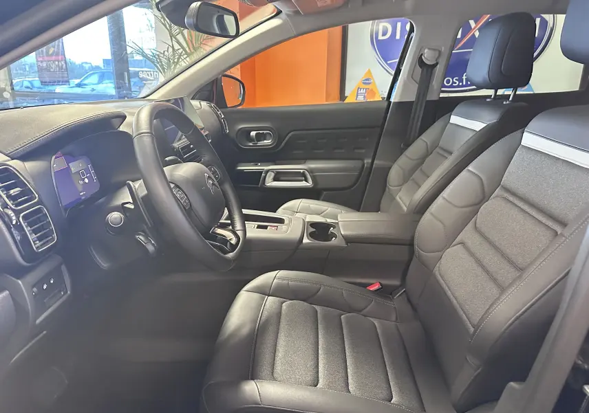 Vue intérieure côté conducteur du Citroën C5 Aircross hybride 2025, sièges en tissu noir et volant cuir avec console centrale.