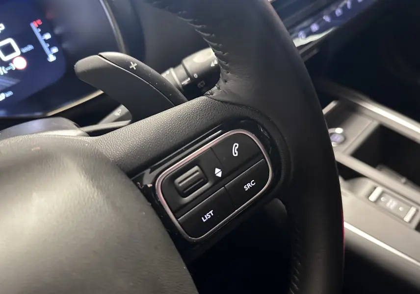 Gros plan sur les commandes noires du volant en cuir du Citroën C5 Aircross hybride 2025, avec palettes de changement de vitesse.