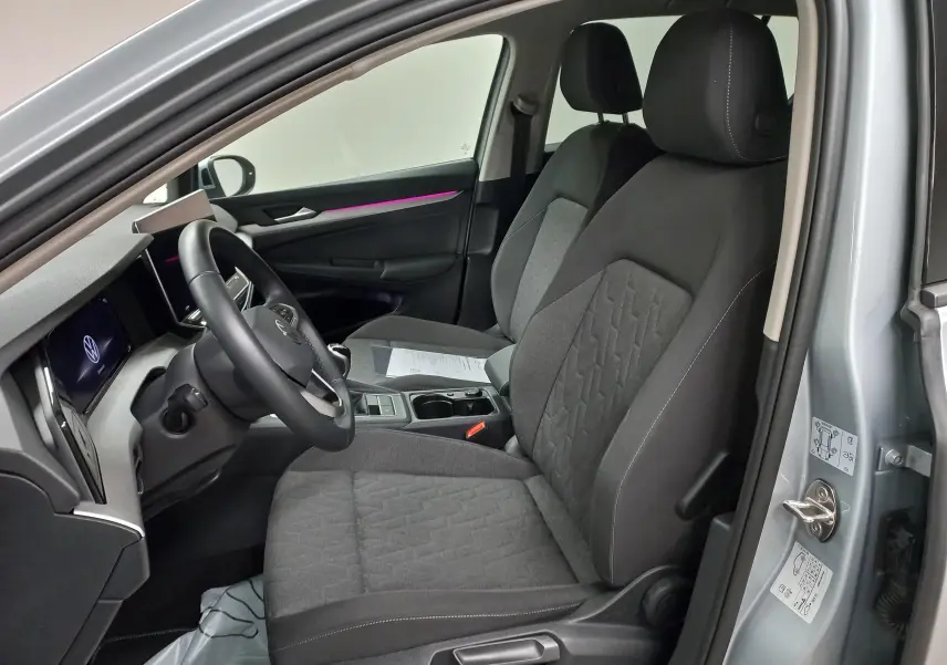 Vue intérieure côté conducteur de la Volkswagen Golf 1.5 eTSI 116 BVM6 argent Dolomite, sièges tissu gris et éclairage d'ambiance violet.