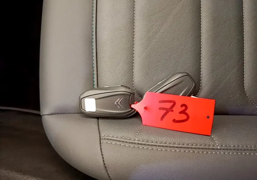 Gros plan sur la clé noire Citroën avec étiquette rouge posée sur un siège en cuir gris foncé.