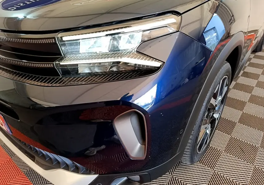 Gros plan sur l'avant droit bleu foncé du Citroën C5 Aircross 2023, mettant en valeur le phare LED et la prise d'air.