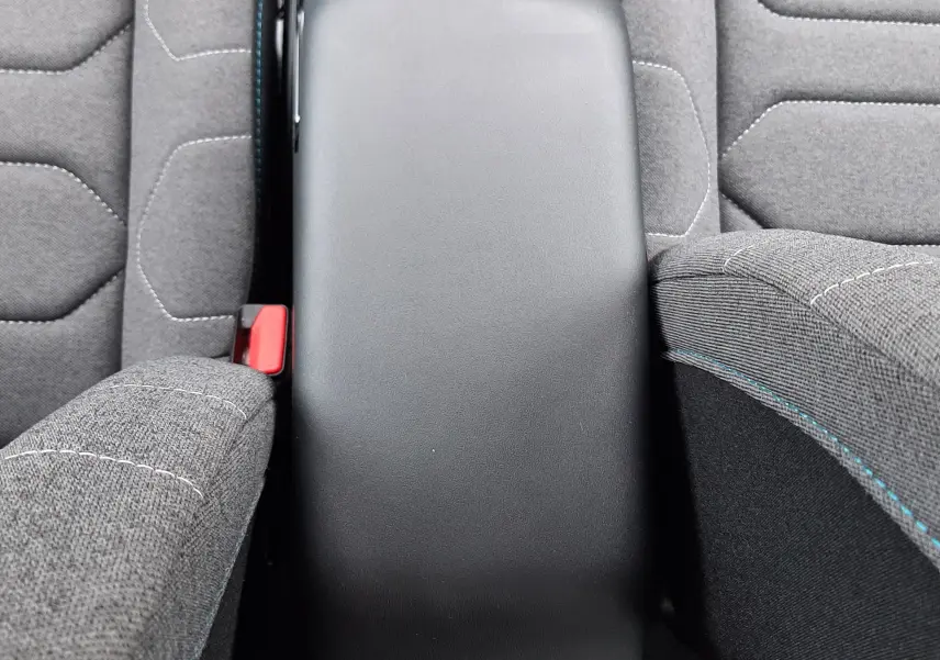 Vue plongeante sur l'accoudoir central noir et les sièges tissu gris avec surpiqûres bleues de la Citroën C4 Hybrid 2024.