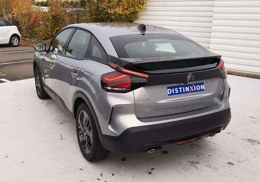 Vue 3/4 arrière droite d'une Citroën C4 gris acier 2024 avec feux arrière LED et toit noir contrasté.