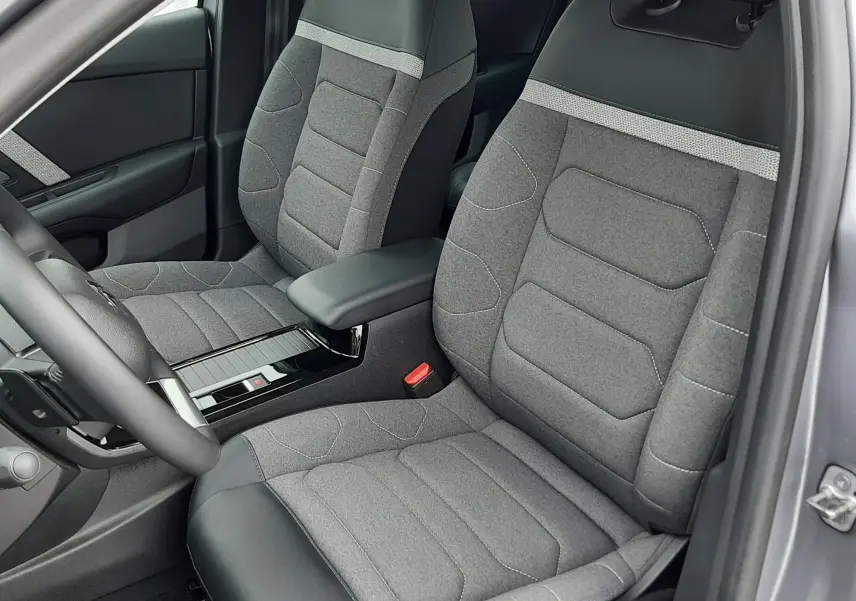 Vue intérieure côté conducteur de la Citroën C4 Hybrid 2024, sièges tissu gris avec surpiqûres et accoudoir central.