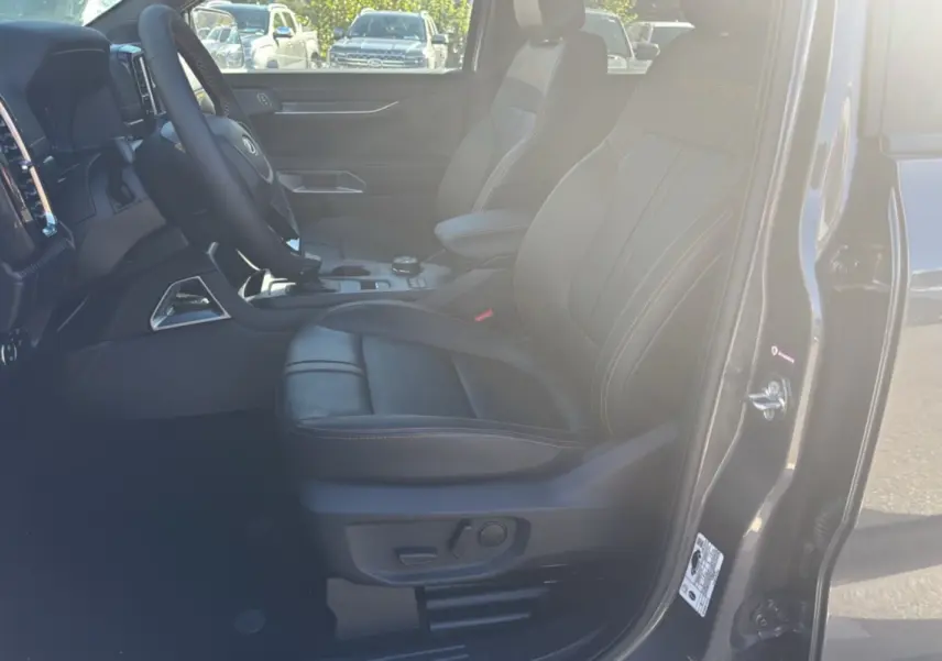 Vue intérieure côté conducteur du Ford Ranger 2025 gris carbone, sièges en cuir Wildtrak avec surpiqûres orange visibles.
