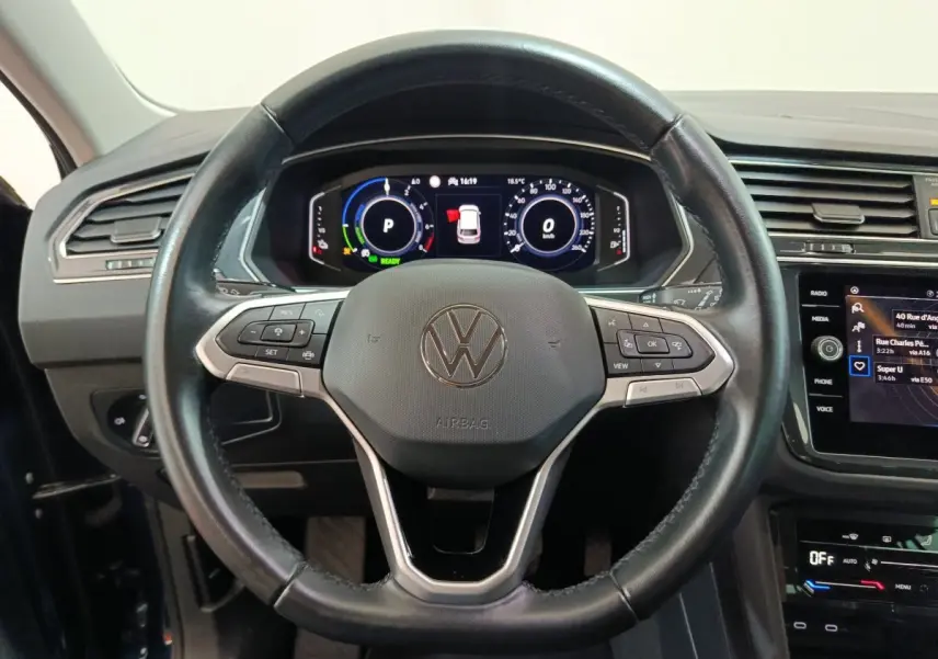 Vue rapprochée du volant cuir noir et du tableau de bord numérique du Volkswagen Tiguan hybride rechargeable bleu 2022.