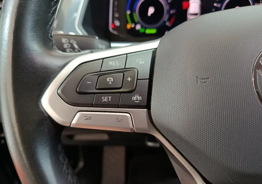 Gros plan sur les commandes du volant cuir à gauche du Volkswagen Tiguan bleu hybride rechargeable 2022.