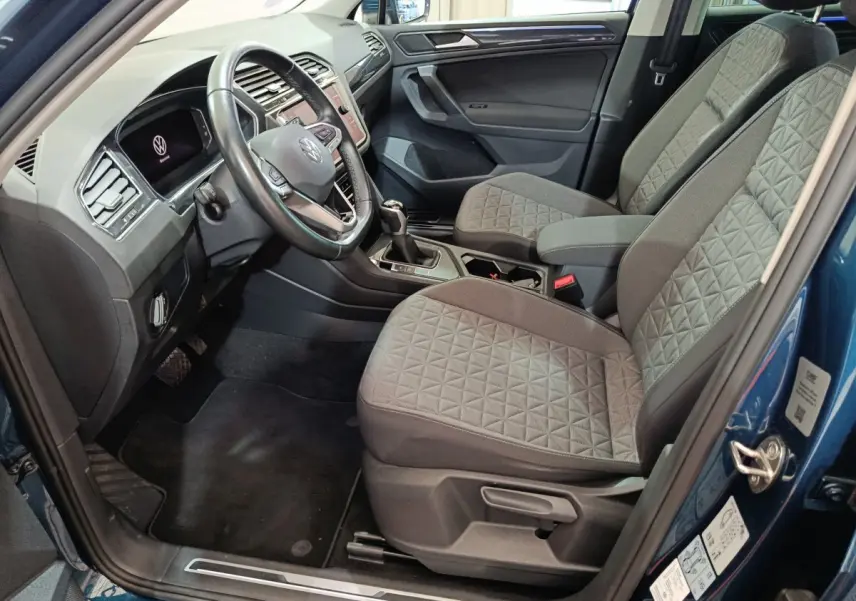 Intérieur côté conducteur du Volkswagen Tiguan bleu 2022, sièges tissu gris et tableau de bord moderne avec écran tactile.