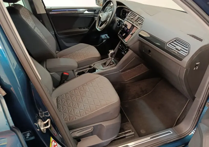 Intérieur côté conducteur du Volkswagen Tiguan bleu 2022, montrant sièges tissu gris et tableau de bord moderne.