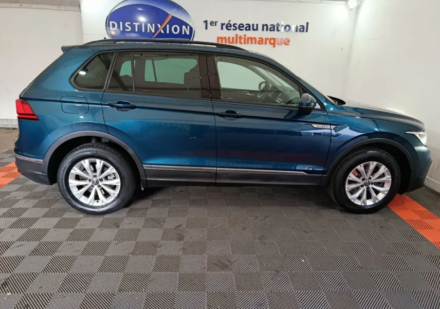 Profil côté gauche du Volkswagen Tiguan bleu 2022 hybride rechargeable, finition Life Business, en intérieur showroom.