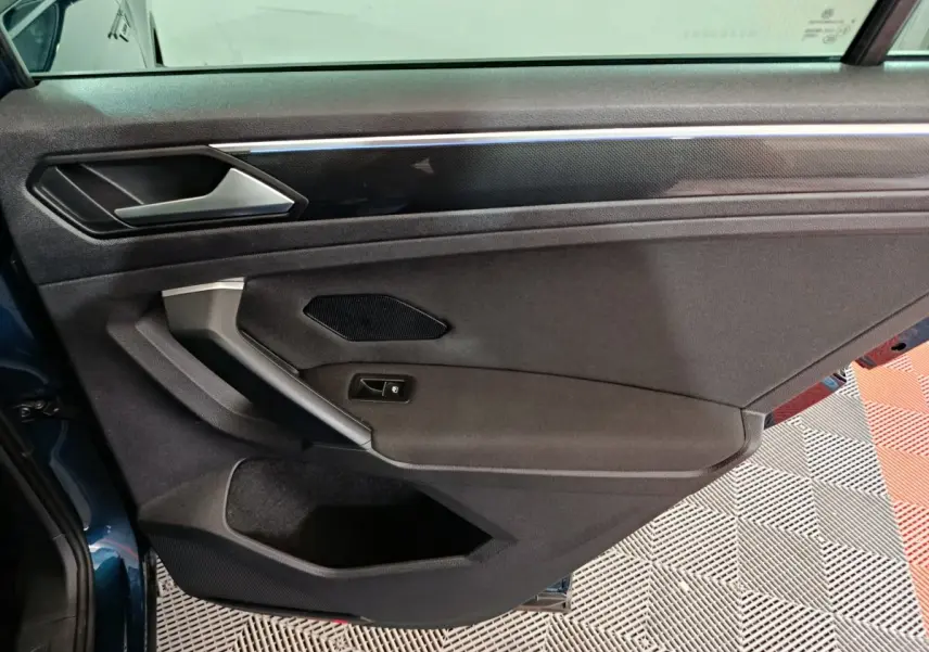 Gros plan sur la porte côté gauche du Volkswagen Tiguan bleu 2022, avec garniture noire et poignée argentée.