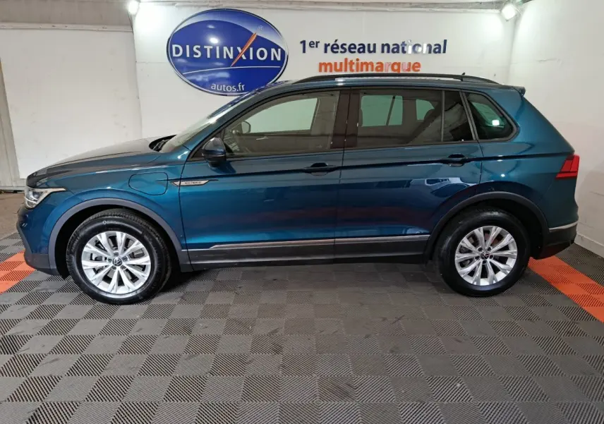 Profil côté gauche d'un Volkswagen Tiguan bleu hybride rechargeable 2022, avec jantes alliage et badge "Hybrid" sur aile avant.