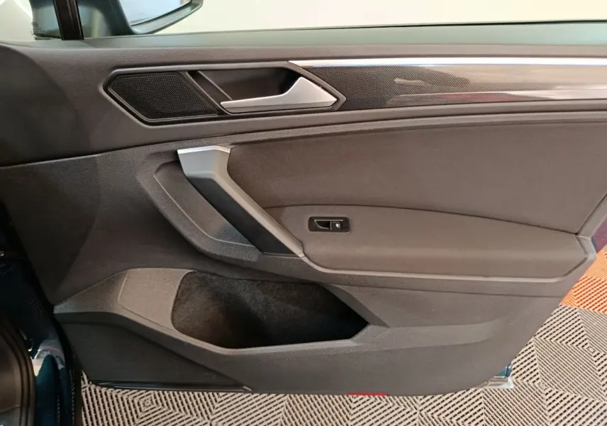 Gros plan sur la porte côté gauche du Volkswagen Tiguan bleu 2022, mettant en valeur la poignée et les finitions intérieures noires.