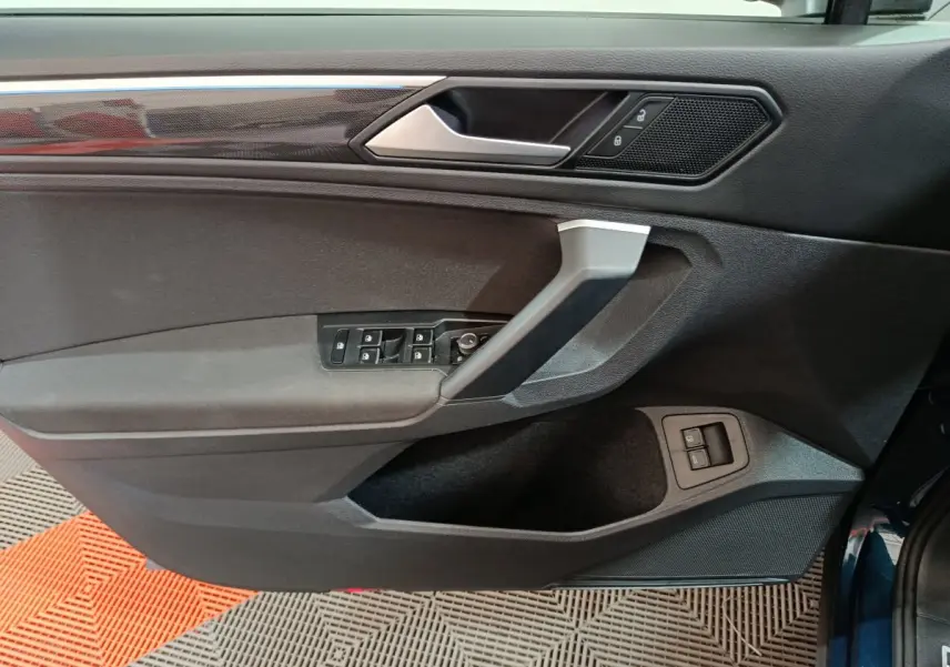 Vue rapprochée de la porte avant gauche du Volkswagen Tiguan bleu 2022, avec commandes électriques et finition noire.