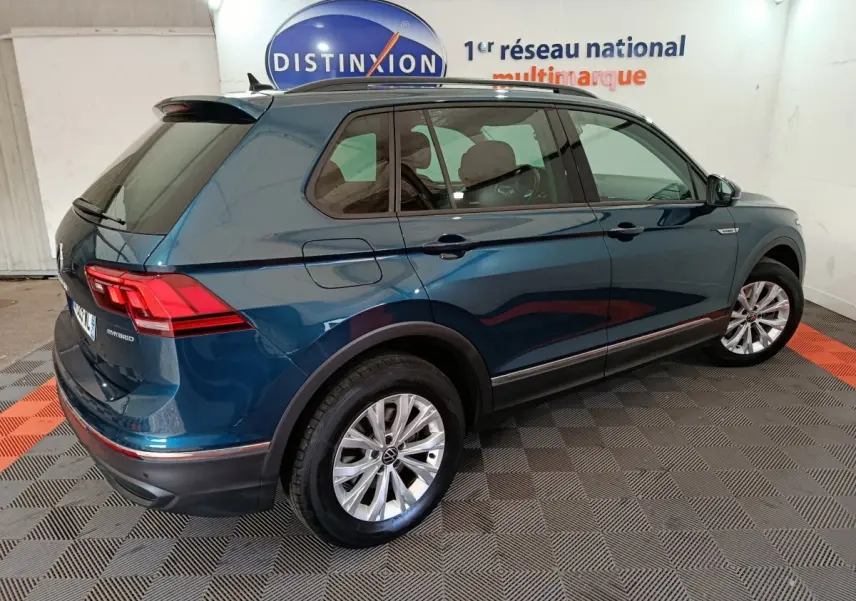 Vue 3/4 arrière droite d'un Volkswagen Tiguan bleu hybride rechargeable avec jantes argentées et toit noir en intérieur showroom.