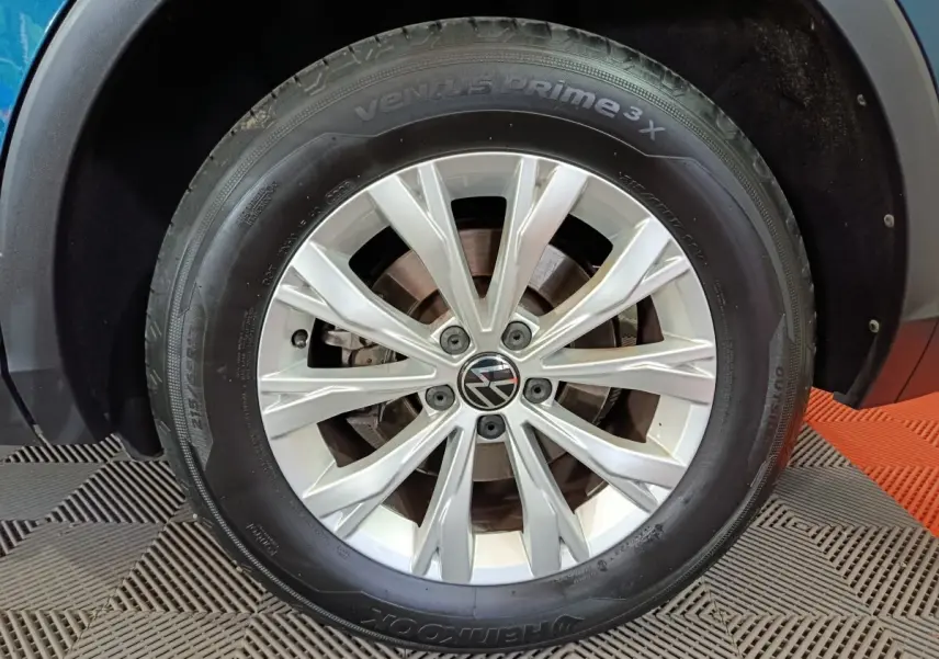 Gros plan sur la roue avant gauche du Volkswagen Tiguan bleu, mettant en valeur la jante argentée et le logo VW central.