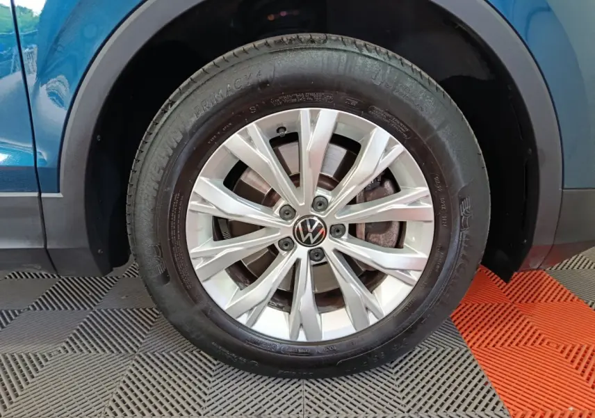 Gros plan sur la roue avant gauche d’un Volkswagen Tiguan bleu 2022 avec jante alliage argentée et logo VW central