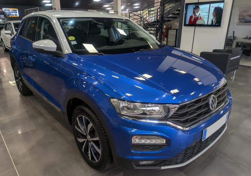 Volkswagen T-Roc bleu Ravenna avec toit blanc, vue 3/4 avant droit en showroom lumineux.