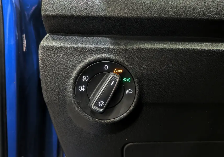 Gros plan sur le bouton de réglage des phares du Volkswagen T-Roc bleu Ravenna, avec fonction automatique activée.