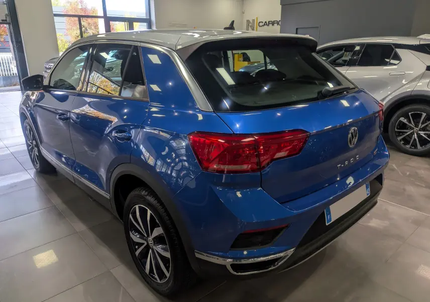 Vue 3/4 arrière droite du Volkswagen T-Roc bleu Ravenna avec toit blanc, soulignant ses feux arrière et jantes biton.