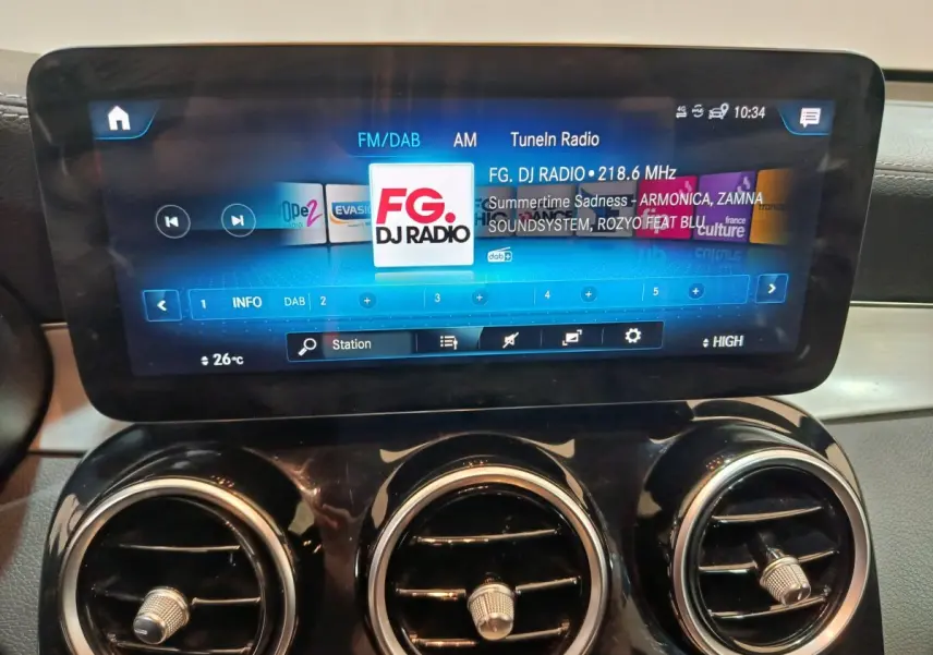 Écran tactile central allumé avec radio FM, entouré de trois aérateurs ronds dans l’habitacle du Mercedes GLC bleu.