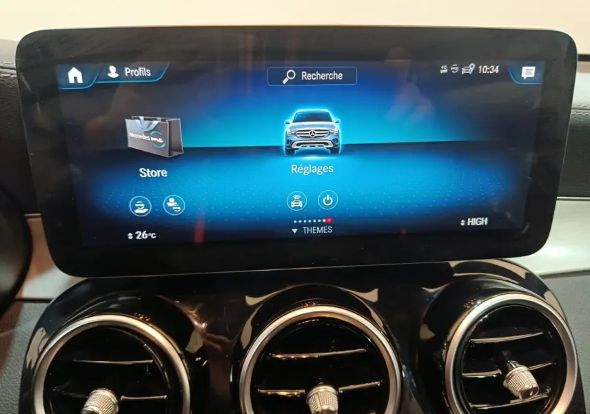 Écran tactile central affichant le menu Réglages sur le tableau de bord du Mercedes GLC 300 E bleu, avec aérateurs ronds chromés.