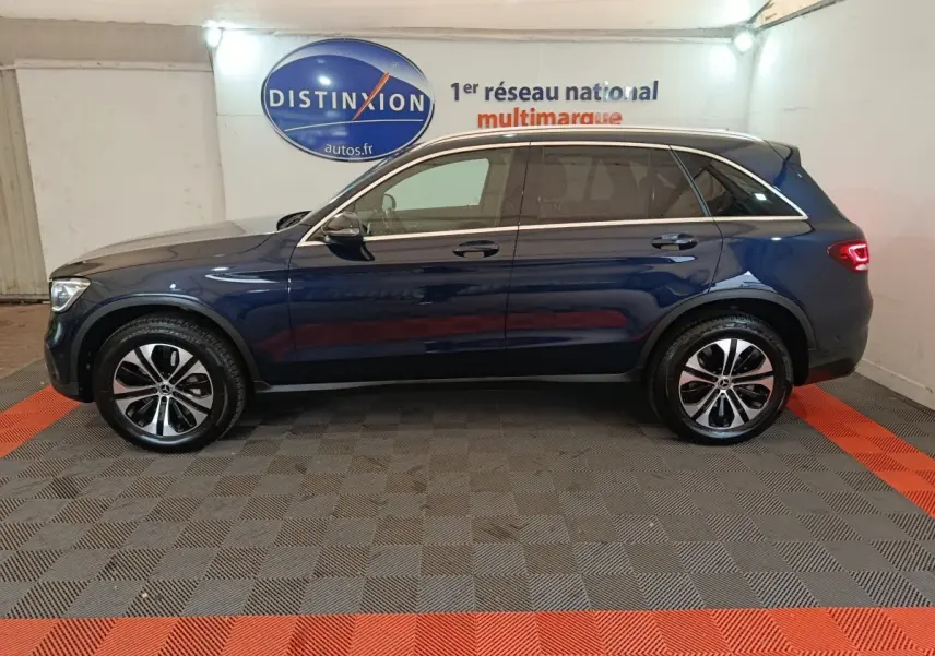 Profil côté gauche d'un Mercedes GLC 300 E Business Line bleu, hybride rechargeable, en intérieur showroom.