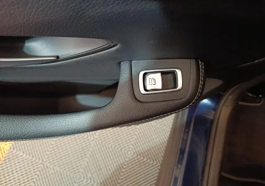Gros plan sur la commande de lève-vitre côté conducteur, garniture cuir noire et bord bleu métallisé visible.