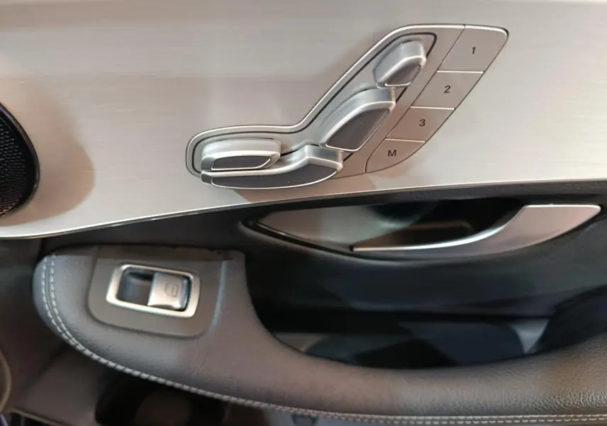 Détail des commandes de réglage de siège en aluminium brossé sur la porte côté gauche d’un Mercedes GLC bleu 2021.