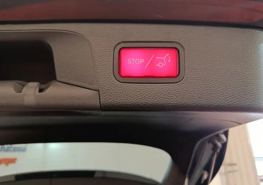 Bouton rouge d'arrêt électrique du coffre visible sur le bord intérieur du hayon d'un Mercedes GLC bleu hybride rechargeable.